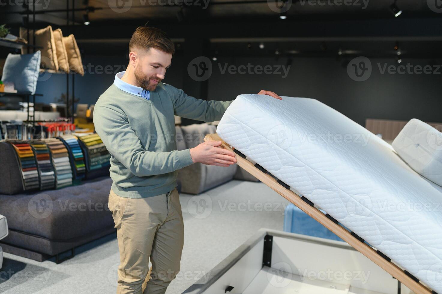 Young male customer examining orthopedic mattress on sale at furniture store, copy space photo