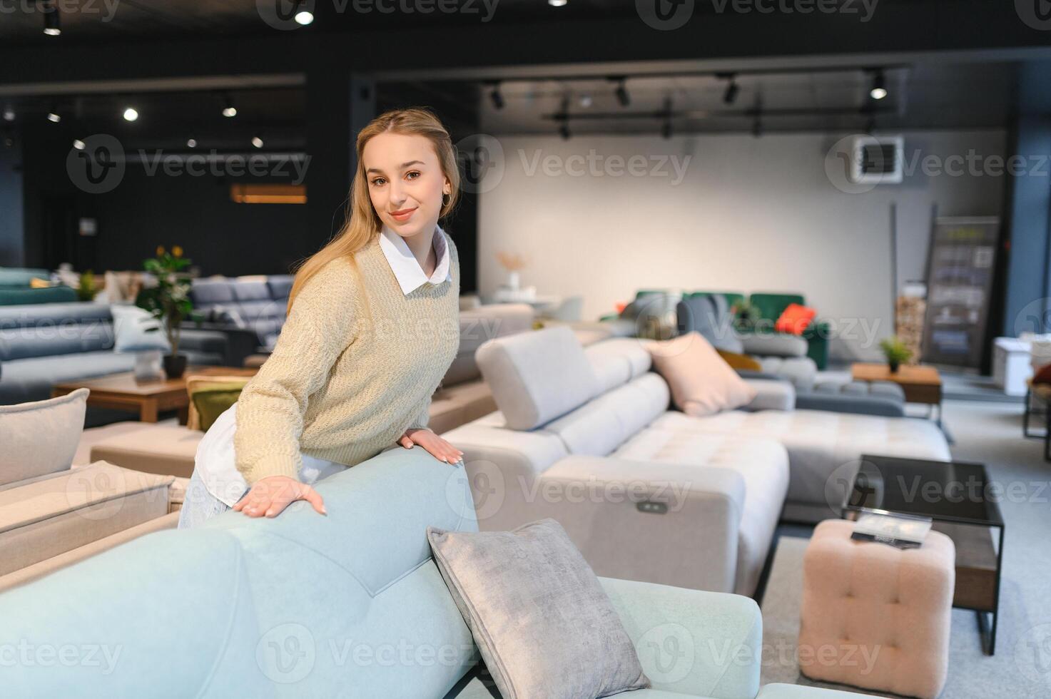 Happy young woman chooses sofa for home in furniture store photo