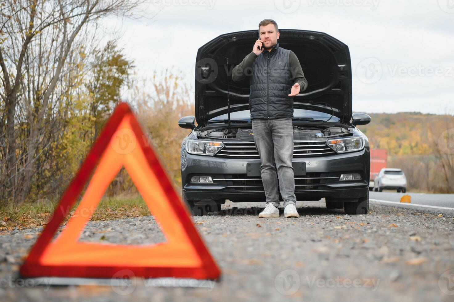 Handsome young man calling for assistance with his car broken down by the roadside photo