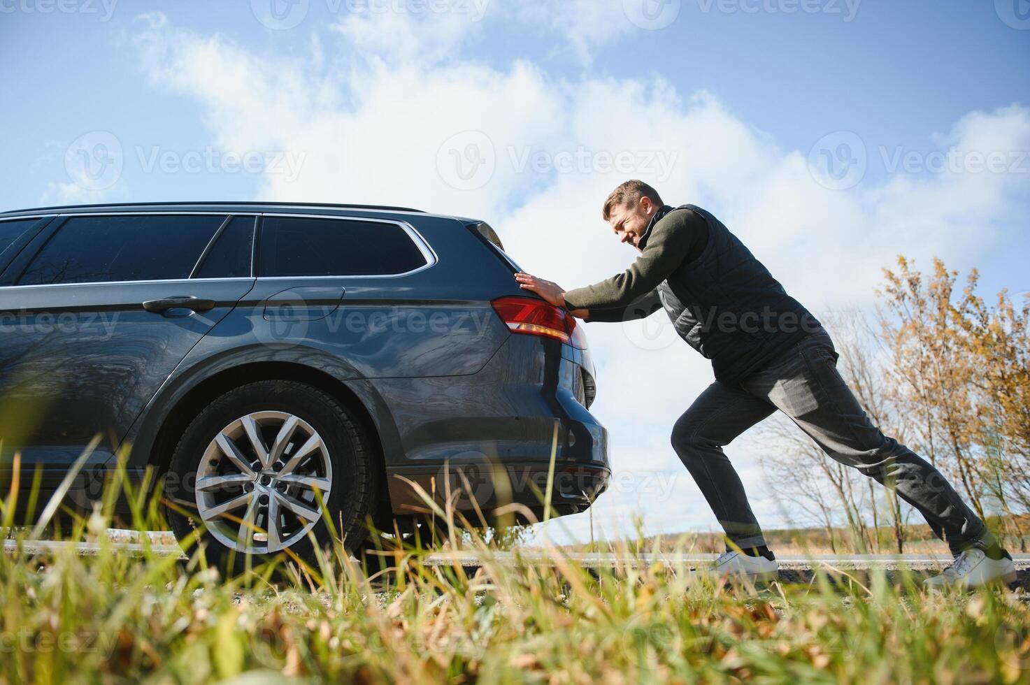 Man pushing a broken car down the rock road photo