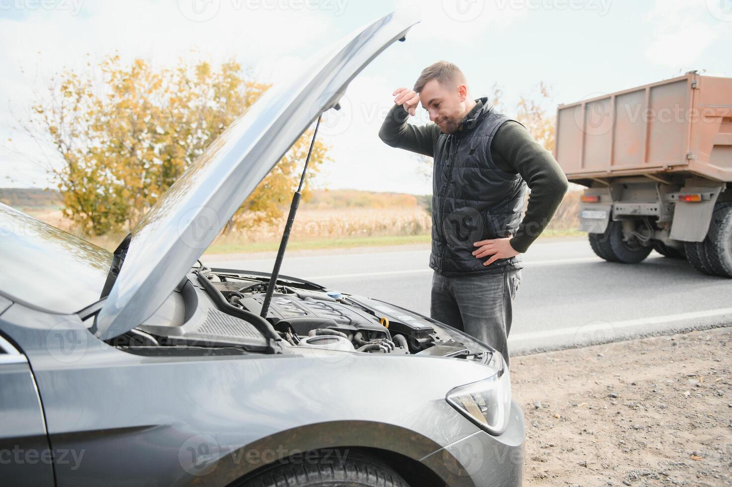 driver trying to figure out how to fix broken down car with red triangle to warn other road users photo