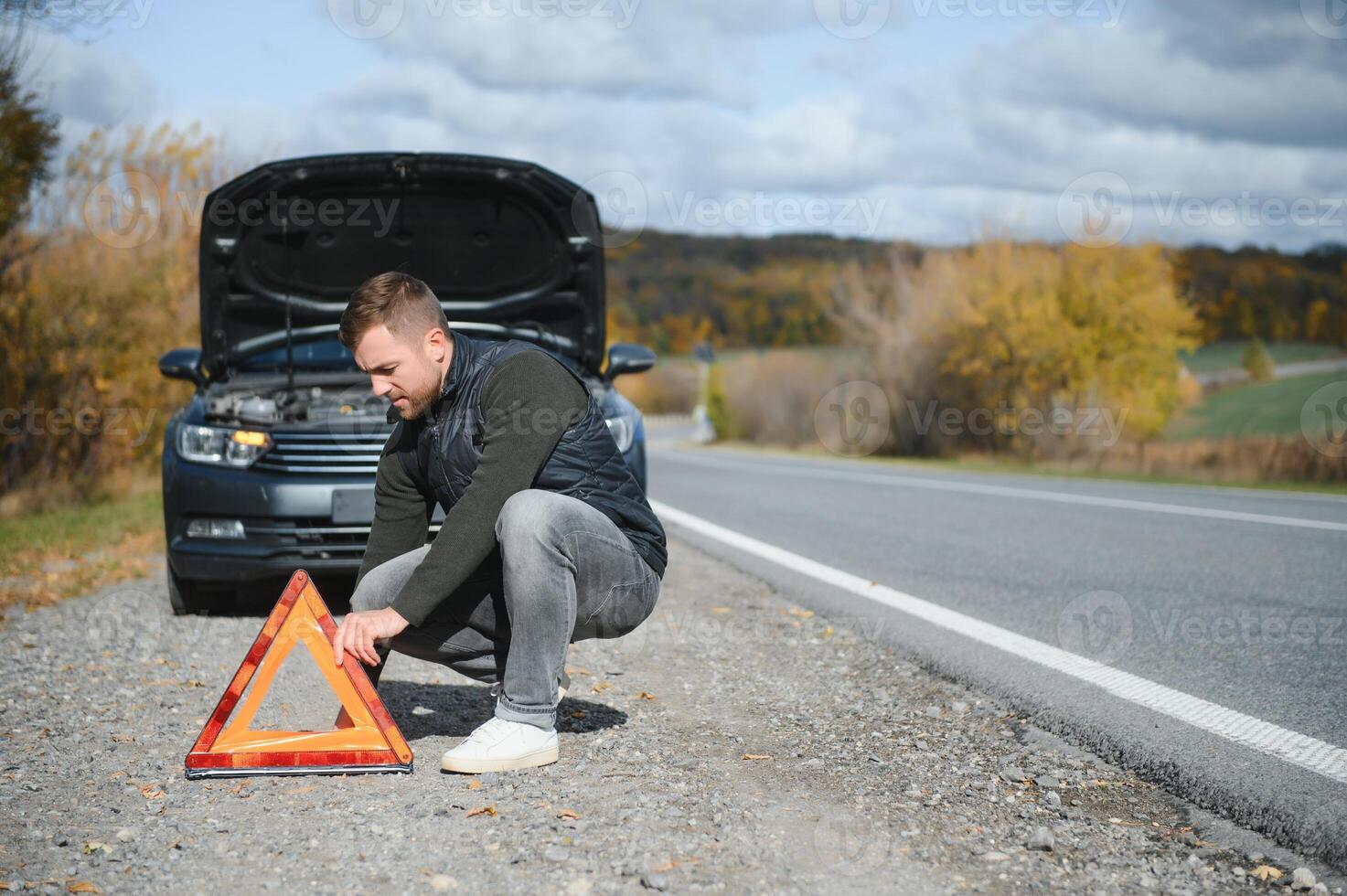 Man repairing a broken car by the road. Man having trouble with his broken car on the highway roadside. Man looking under the car hood. Car breaks down on the autobahn. Roadside assistance concept. photo