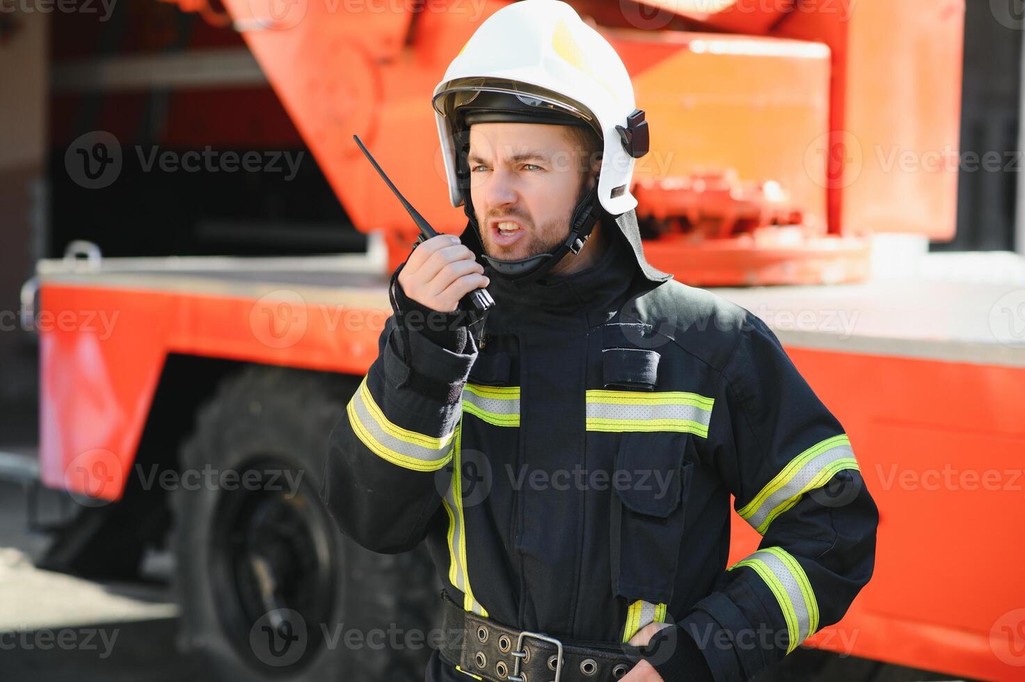 Fireman in a protective uniform standing next to a fire truck and talking on the radio. photo