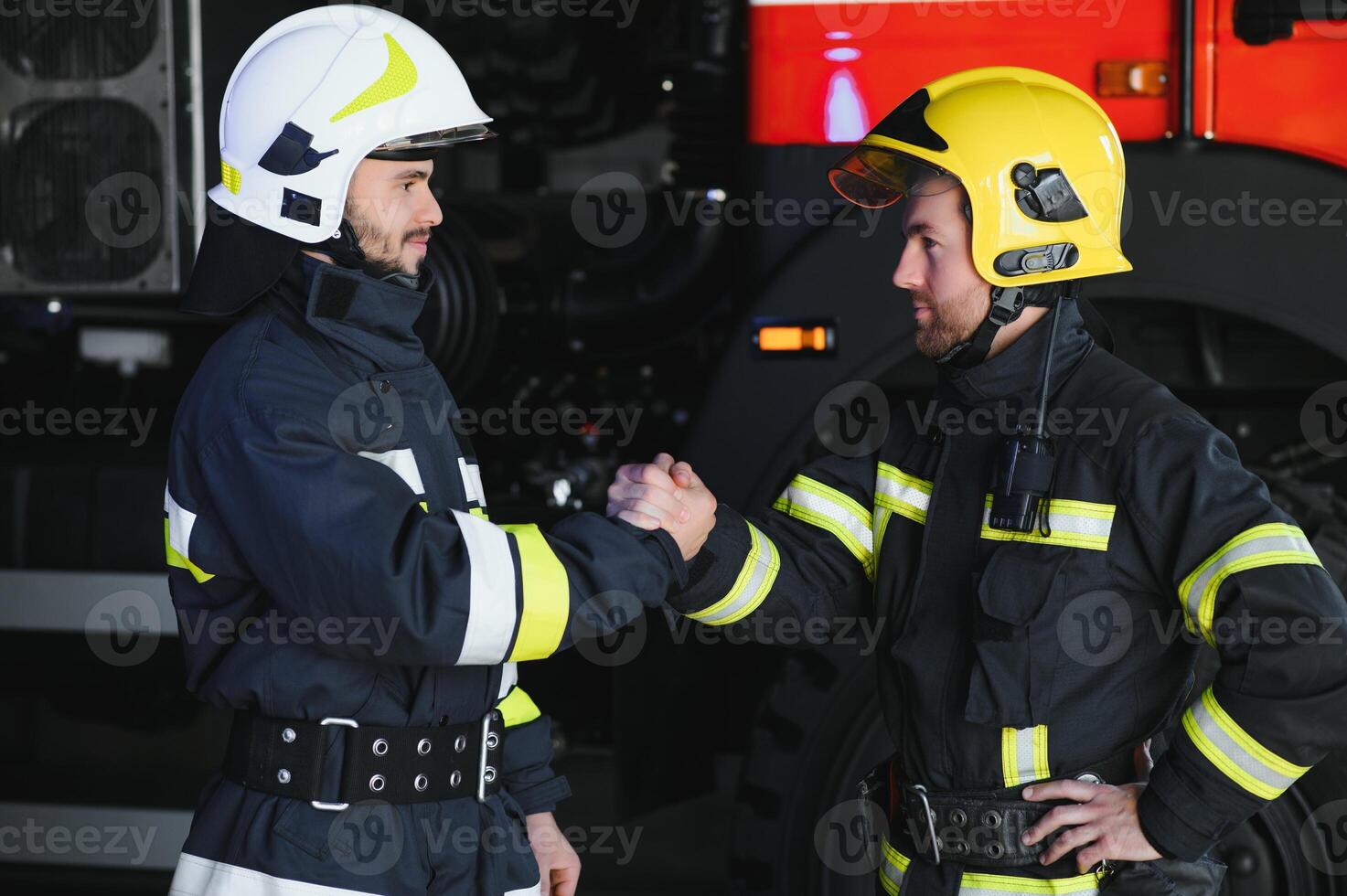Two firefighters in protective clothing in helmets with fire engine, friendly handshake photo