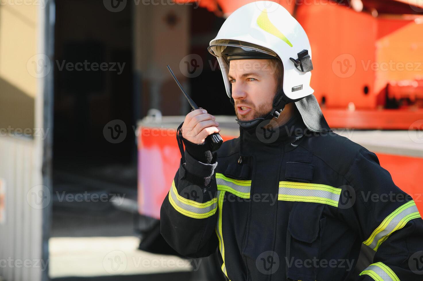 Fireman in a protective uniform standing next to a fire truck and talking on the radio. photo