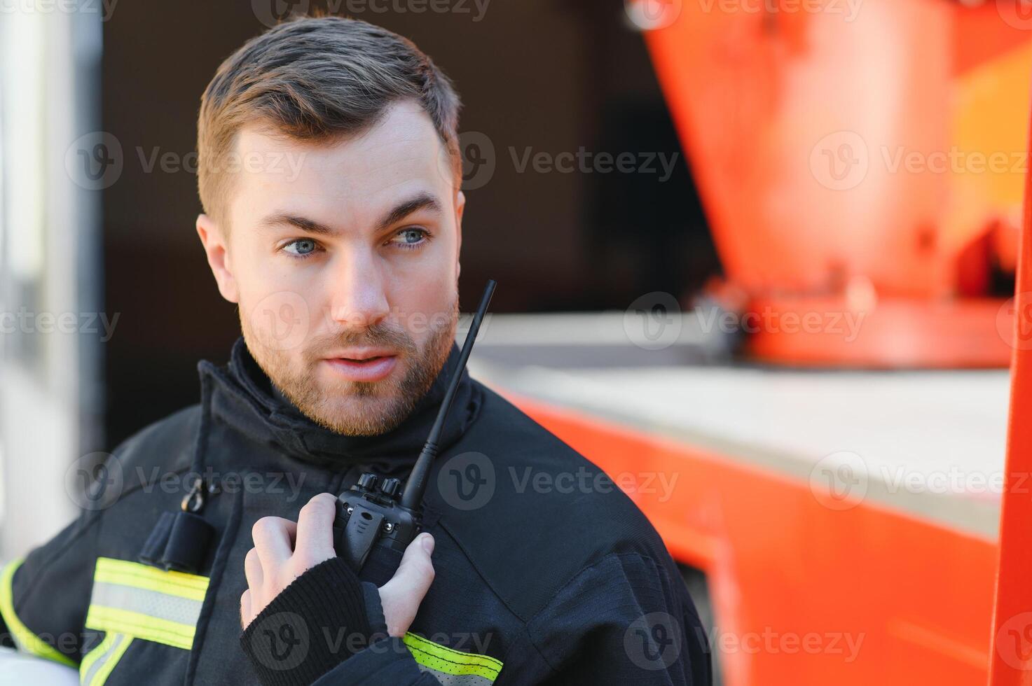 Fireman in a protective uniform standing next to a fire truck and talking on the radio. photo