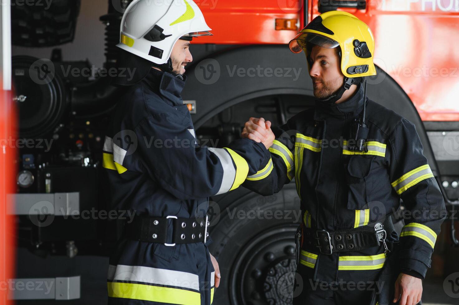 Two firefighters in protective clothing in helmets with fire engine, friendly handshake photo