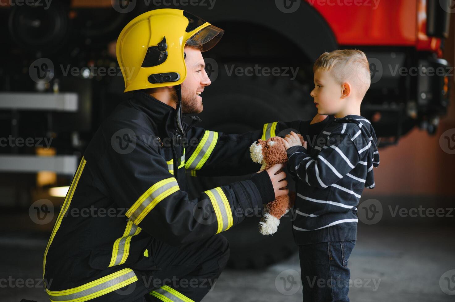 Portrait of rescued little boy with firefighter man standing near fire truck. Firefighter in fire fighting operation. photo