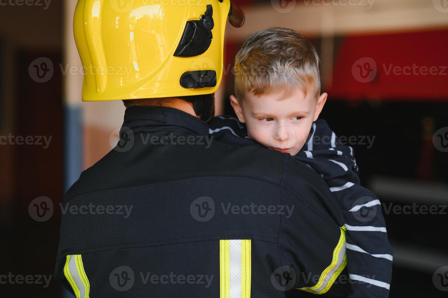 Dirty firefighter in uniform holding little saved boy standing on black background. photo