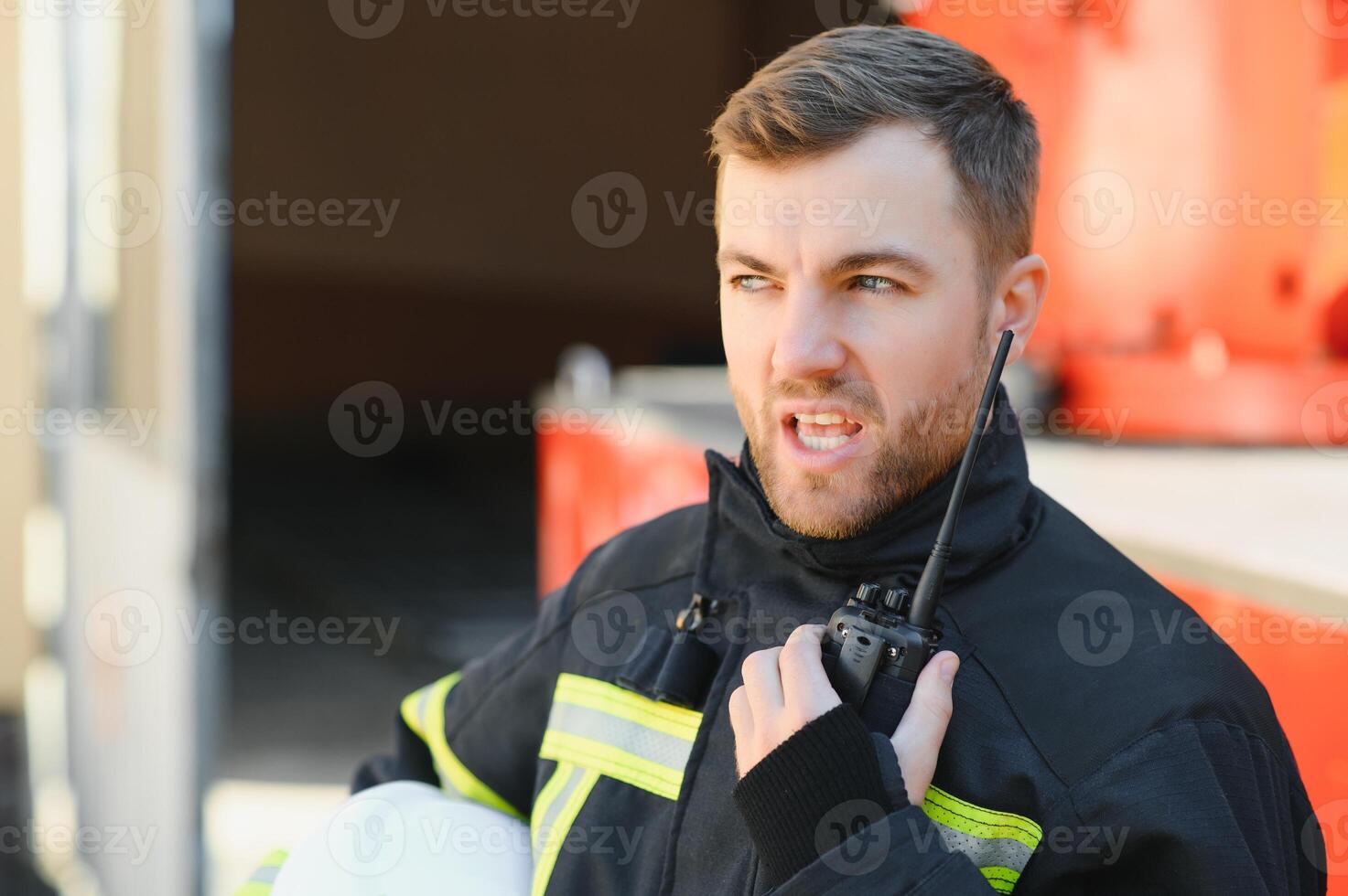 Fireman in a protective uniform standing next to a fire truck and talking on the radio. photo