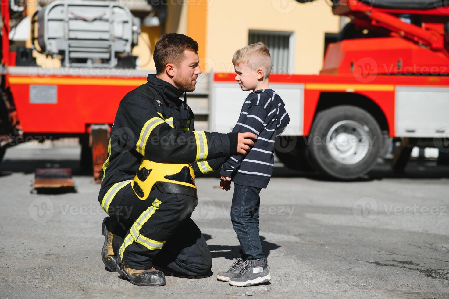 A firefighter take a little child boy to save him. Fire engine car on background. Fireman with kid in his arms. Protection concept. photo