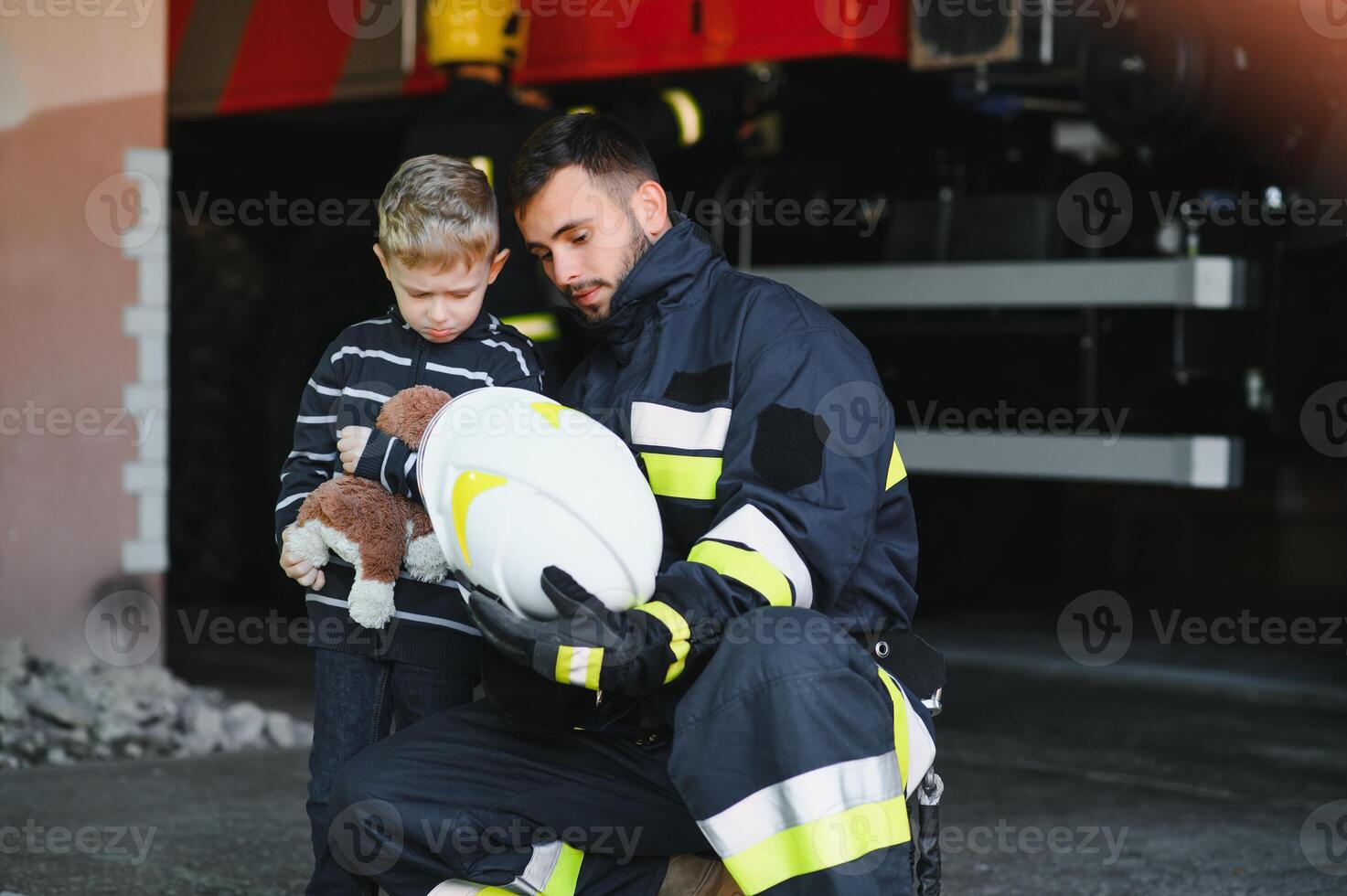 Portrait of rescued little boy with firefighter man standing near fire truck. Firefighter in fire fighting operation. photo