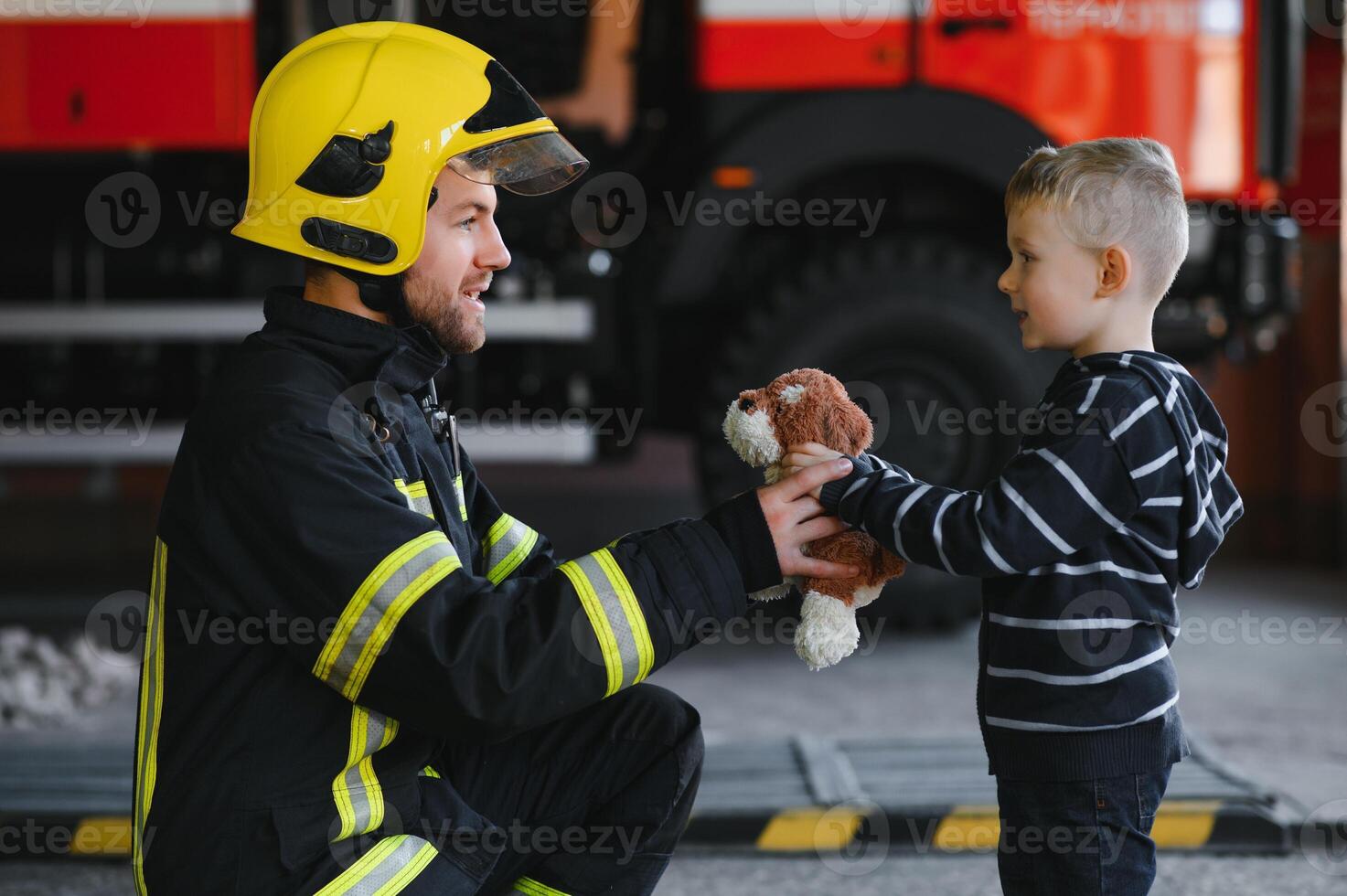 A firefighter take a little child boy to save him. Fire engine car on background. Fireman with kid in his arms. Protection concept. photo