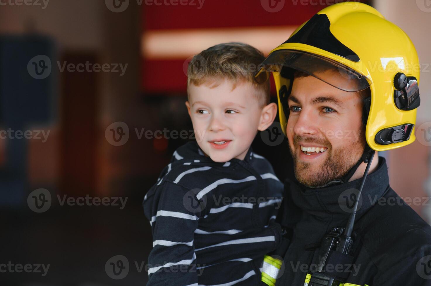 Dirty firefighter in uniform holding little saved boy standing on black background. photo
