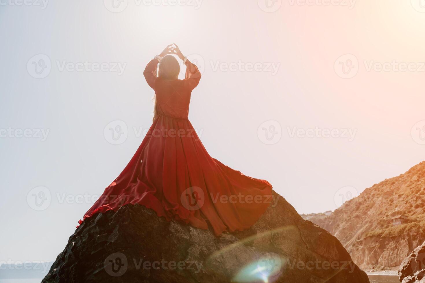 Woman travel sea. Young Happy woman in a long red dress posing on a beach near the sea on background of volcanic rocks, like in Iceland, sharing travel adventure journey photo