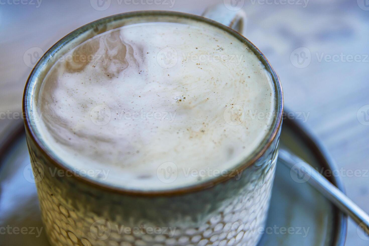 Top view of white cream foam slowly dissolving in the black coffee rotating and mixing in the ceramic mug on the plate with spoon. Latte or macchiato creamy texture. Breakfast. Top view. Close up. photo