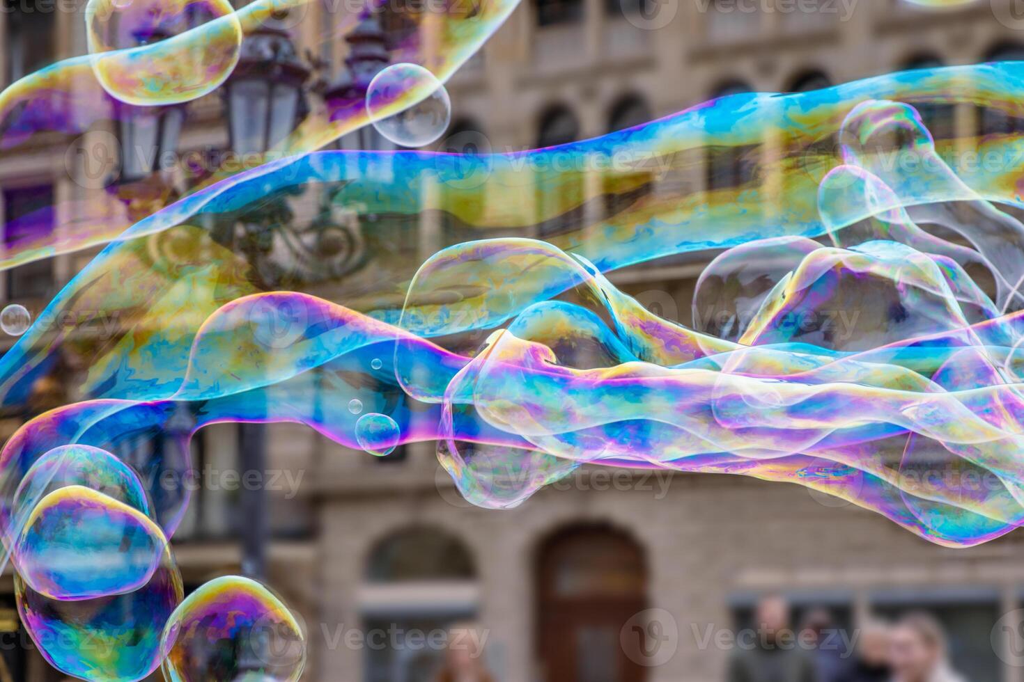 Many multicolored giant soap bubbles flying in the air on a windy day. Huge bubble are stretching on the wind into long smoothy changing form without popping. Close up. Copy space. Selective focus. photo