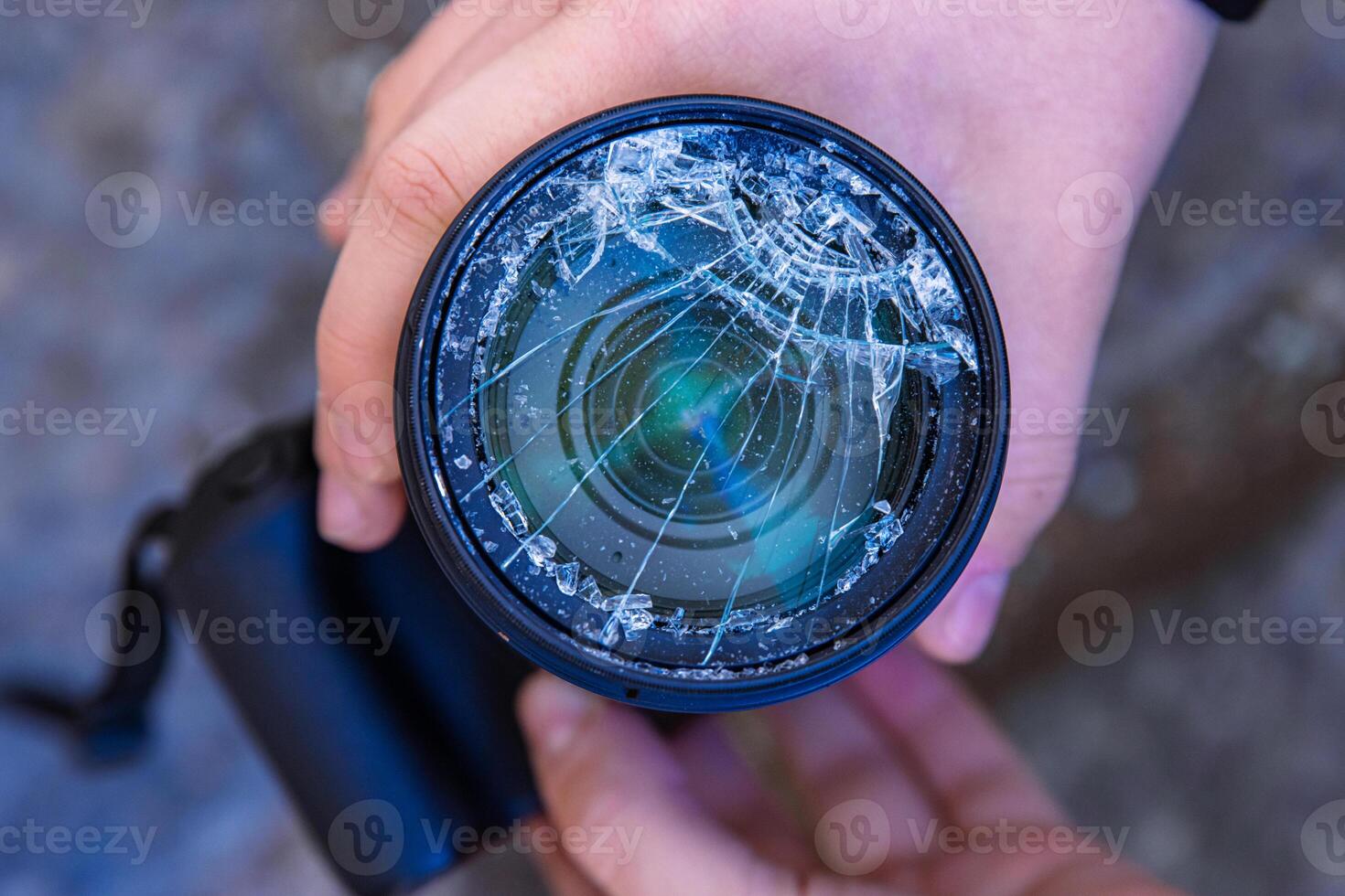 Hands of young photographer holding DSLR photo camera with broken lens filter glass after if fall down onto the floor. Close up. Destroyed cracked photo-filter. Macro. Top view. Selective focus.
