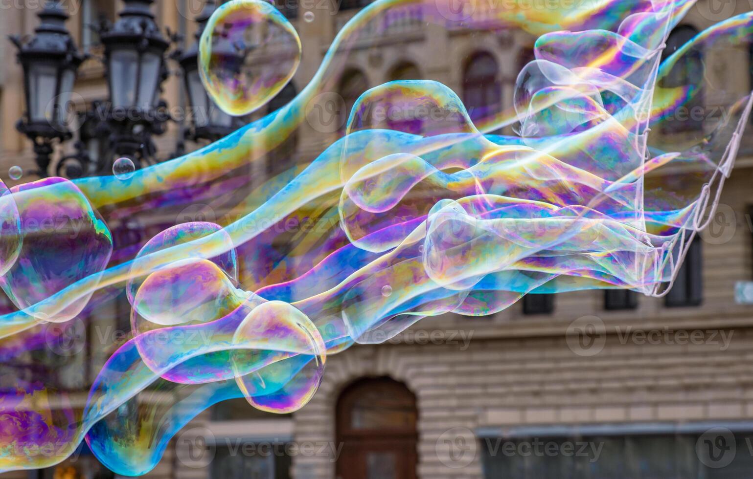 Many multicolored giant soap bubbles flying in the air on a windy day. Huge bubble are stretching on the wind into long smoothy changing form without popping. Close up. Copy space. Selective focus. photo