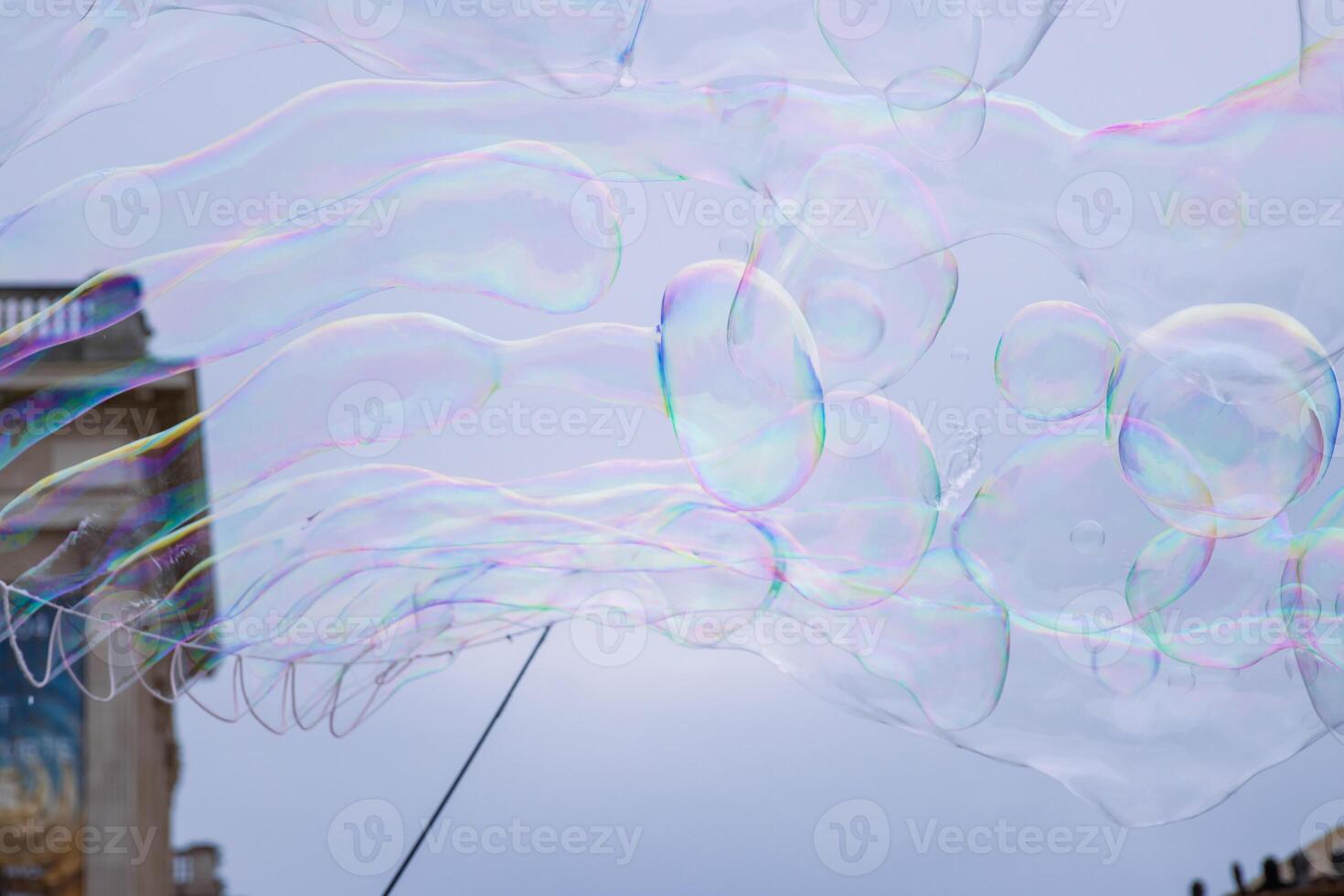 Many multicolored giant soap bubbles flying in the air on a windy day. Huge bubble are stretching on the wind into long smoothy changing form without popping. Close up. Copy space. Selective focus. photo
