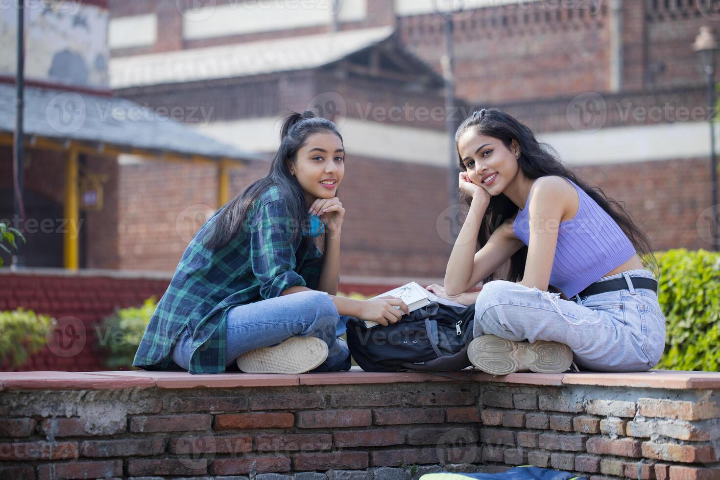 While sitting in the college ground, two innocent ladies hold hands under their chins. photo