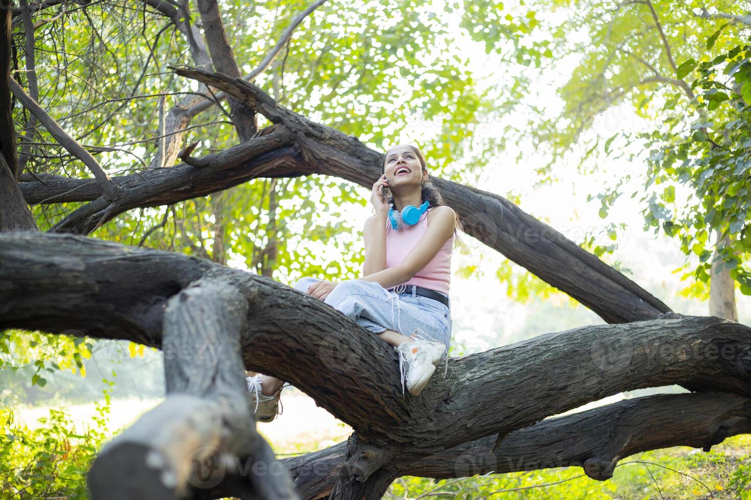 Alone Woman Talking On Phone While Sitting On Tree Branch photo