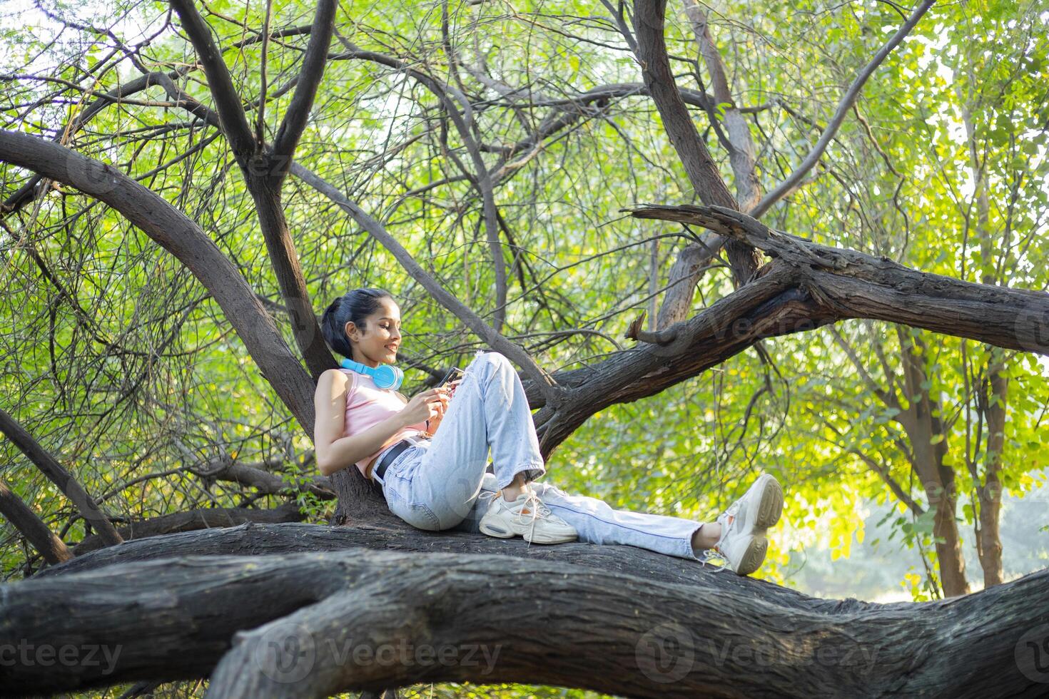 Young Lady is Lying On a Tree Branch and Using Her Smartphone photo