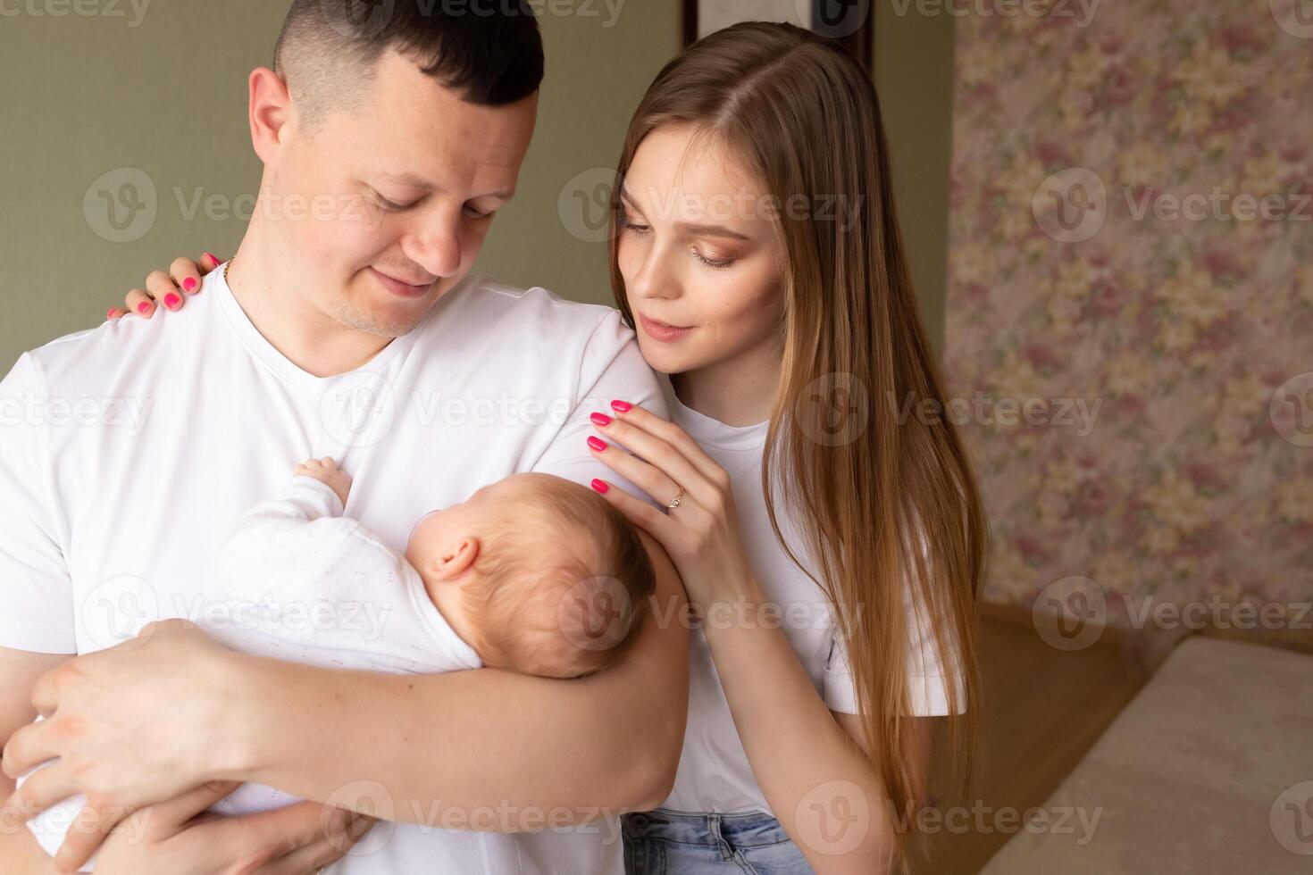 dad holds a baby with a pacifier in his arms close-up portrait of a baby. young parents hold the baby in their arms. dad and mom hug a small child. happy family relaxing at home photo