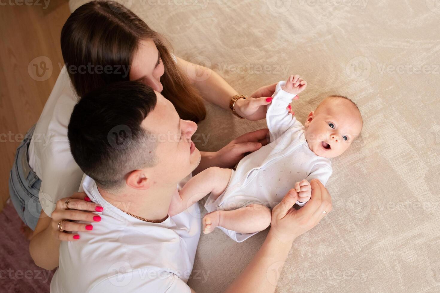 parents play with a baby at home on a bed covered with a linen bedspread. family concept. happy parenthood concept. top view happy parents hugging baby photo