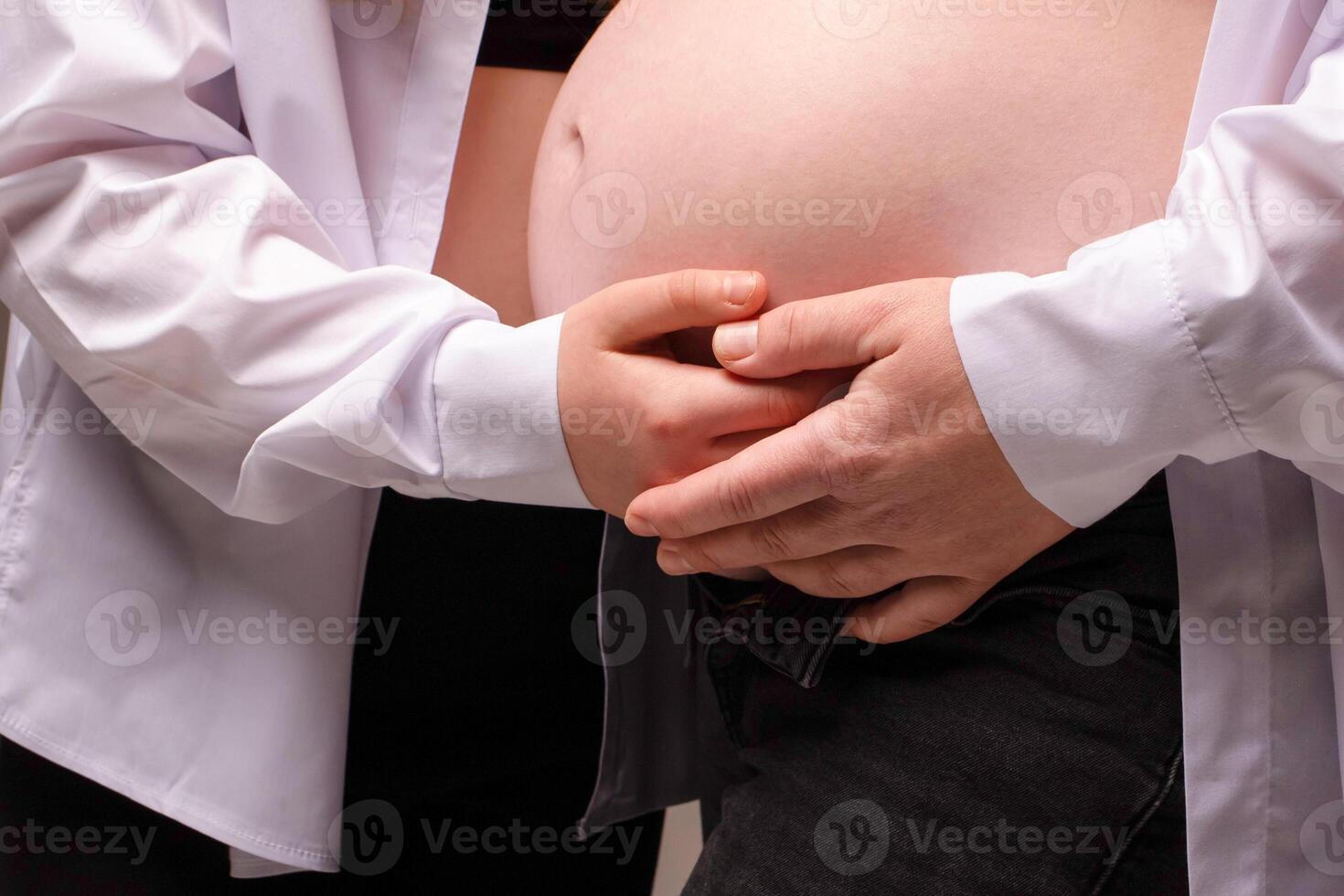 close-up photograph of a pregnant belly being hugged by the hands of mother and baby. family expecting a baby photo