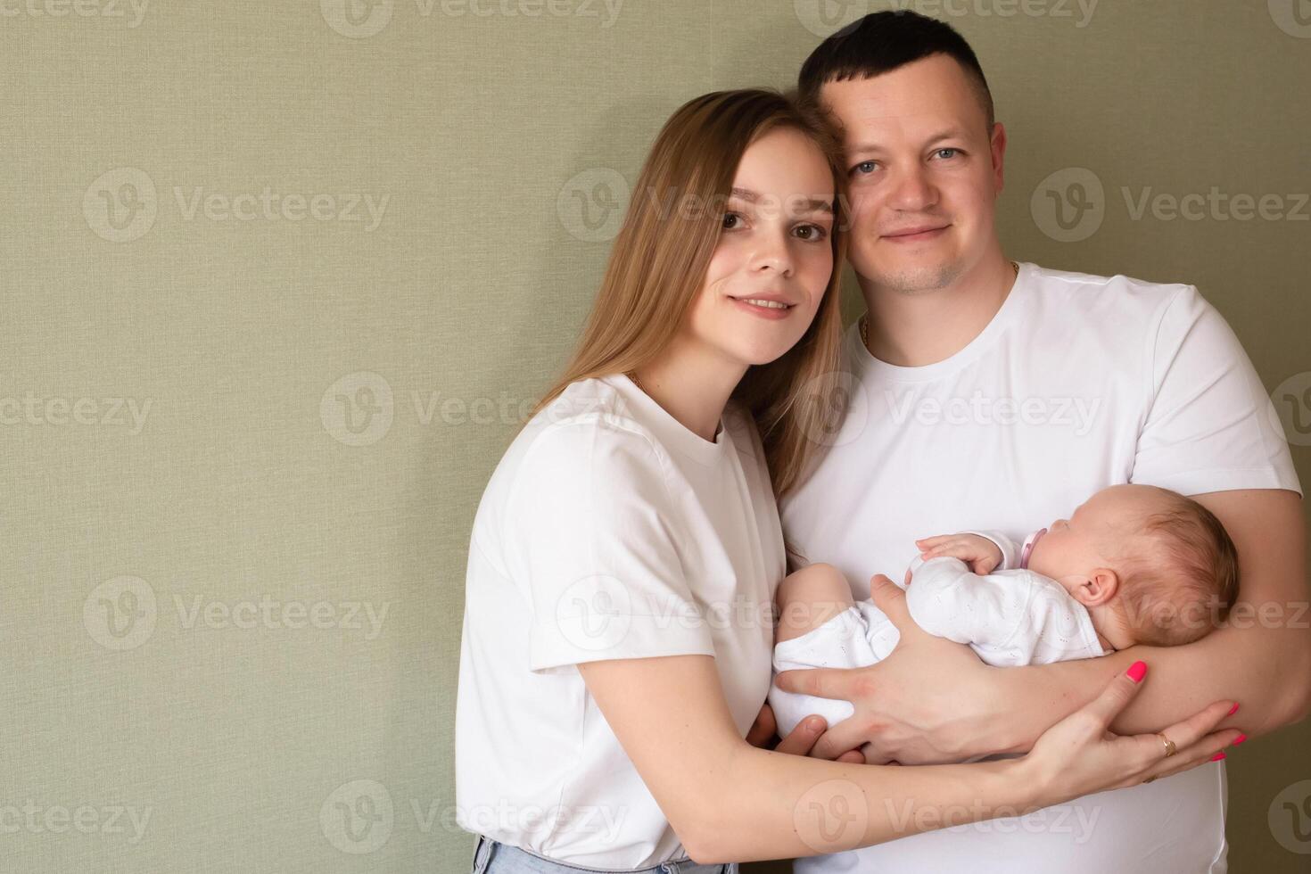 dad holds a baby with a pacifier in his arms close-up portrait of a baby. young parents hold the baby. dad and mom hug a small child. happy family relaxing at home. green background. copy space photo