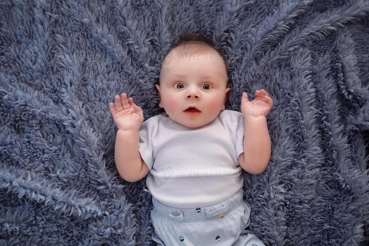 happy beautiful newborn baby boy lying on his back on a blue background. portrait beautiful newborn looks into the frame photo