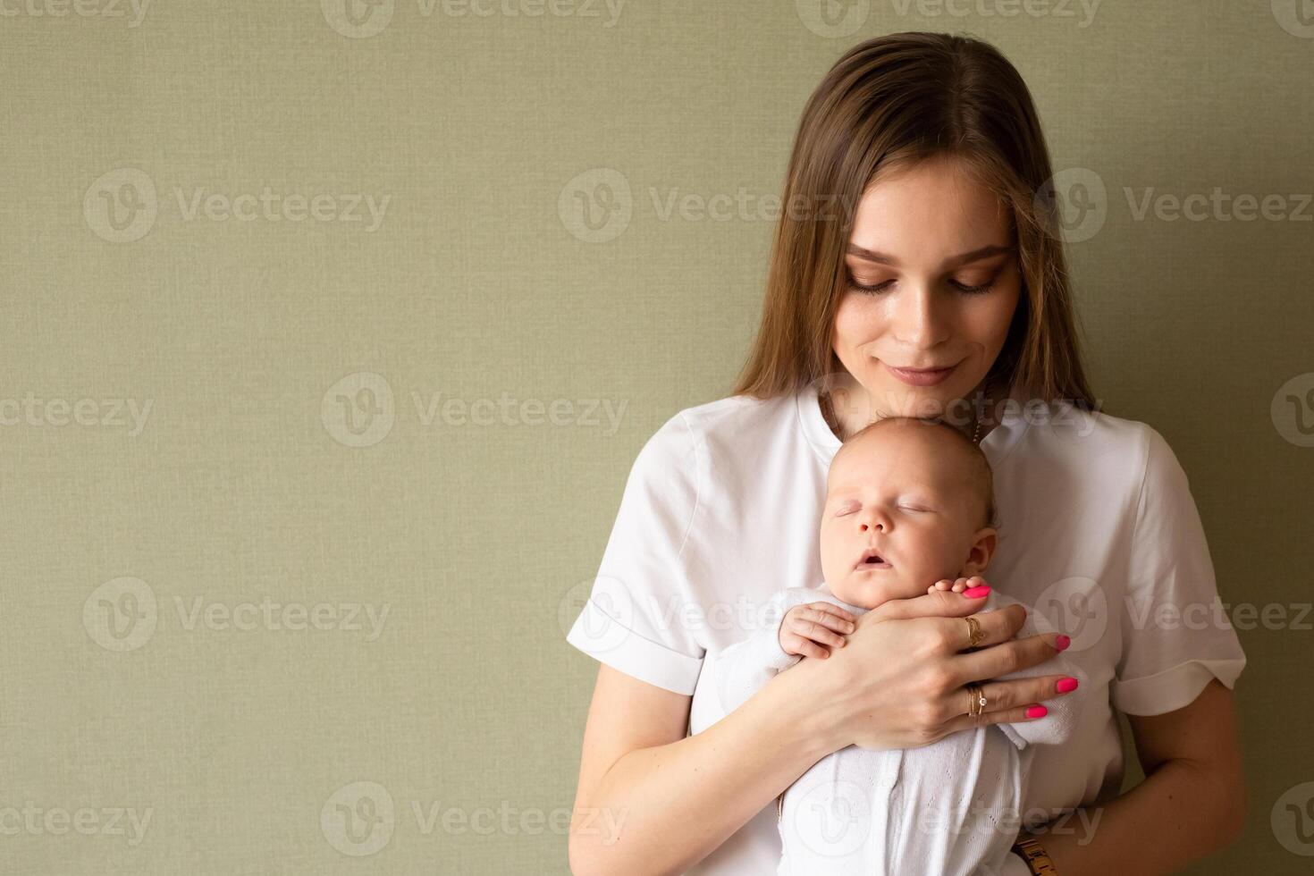 mother holds the baby in her arms and carefully looks at the child on a green background. portrait of a baby in the arms of a parent photo