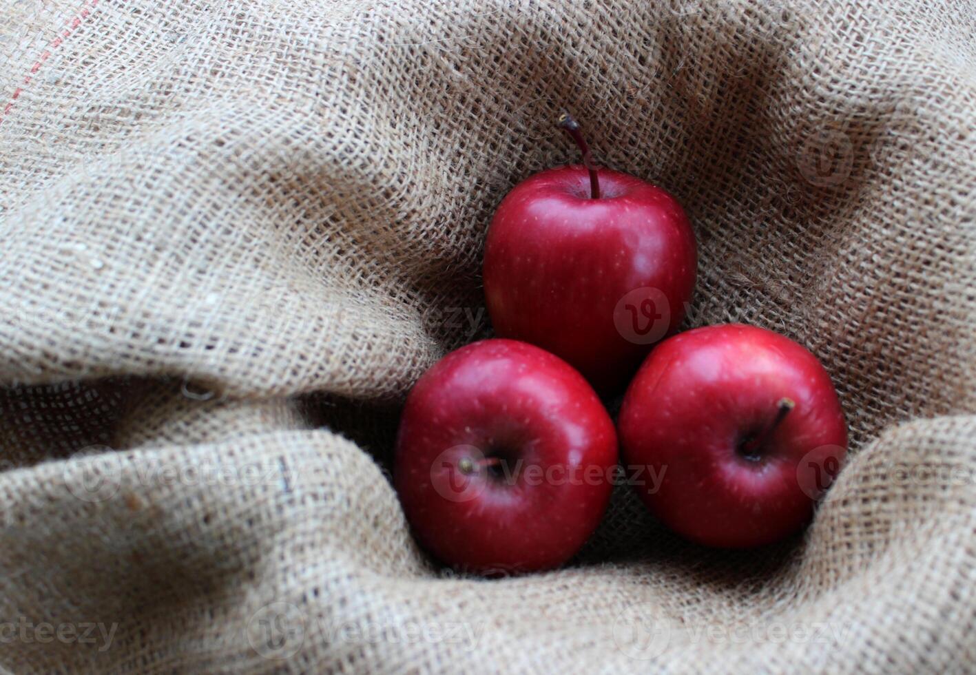 Three red apples in a fruit basket lined with burlap top view photo