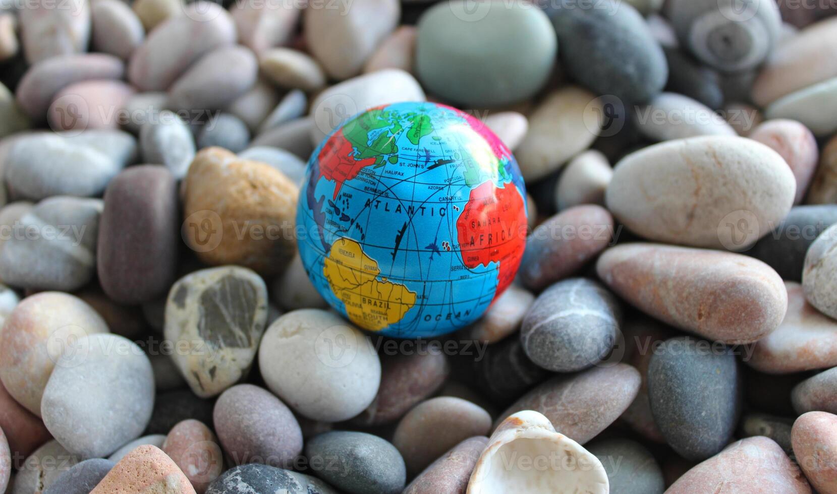 Miniature globe on a sea stones with conventionally drawn continents, oceans and trade routes on it photo