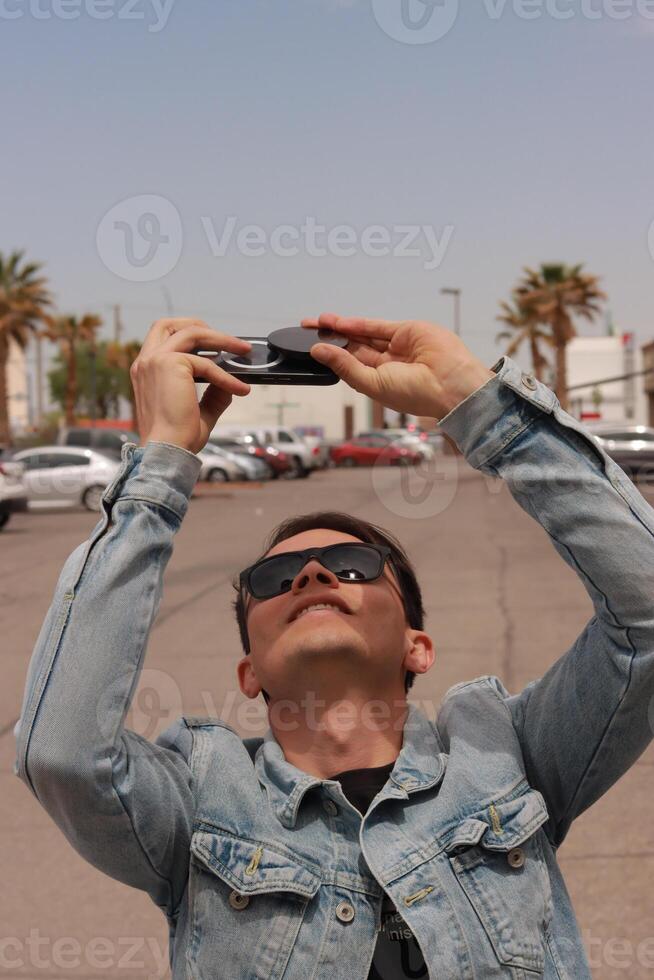 Young Man Looking at the Sun and taking photos During a Solar Eclipse using a Black Obsidian Stone