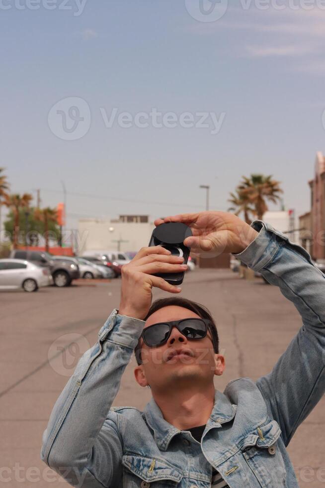 Young Man Looking at the Sun and taking photos During a Solar Eclipse using a Black Obsidian Stone