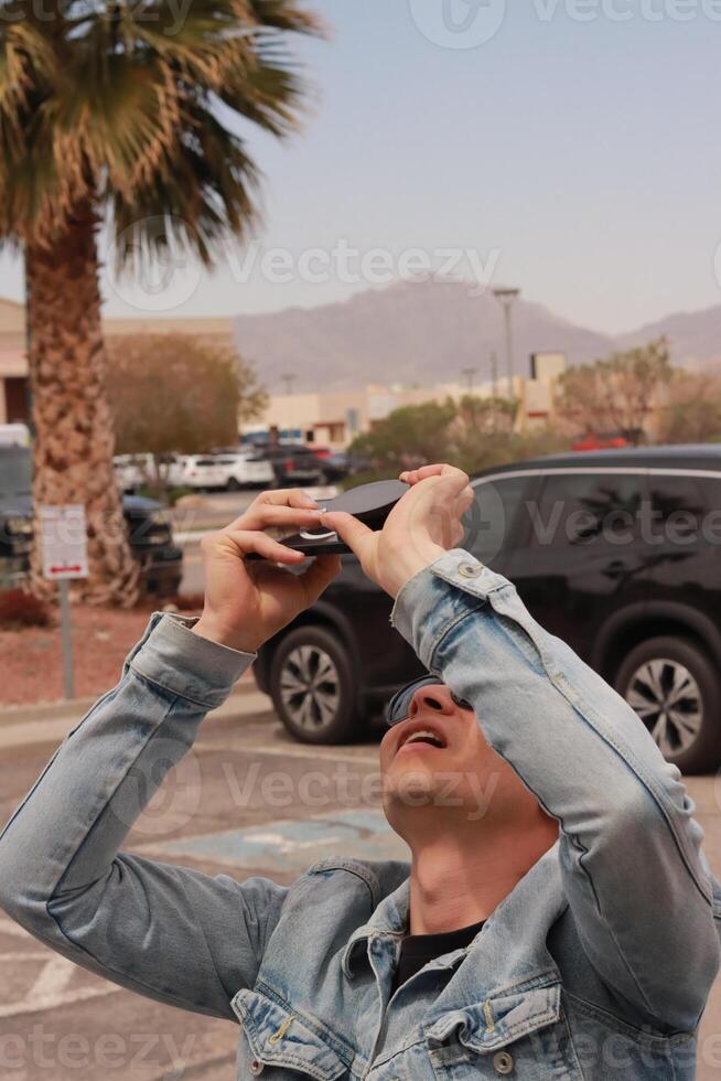 Young Man Looking at the Sun and taking photos During a Solar Eclipse using a Black Obsidian Stone