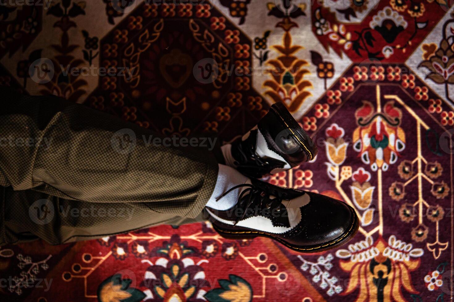Close-up view of two-tone wingtip brogue shoes made of genuine leather worn indoors on the classic red carpet. Concept photo of black and white wingtip brogue shoes with a red Turkish carpet base