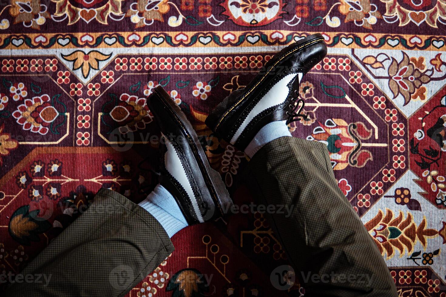 Close-up view of two-tone wingtip brogue shoes made of genuine leather worn indoors on the classic red carpet. Concept photo of black and white wingtip brogue shoes with a red Turkish carpet base