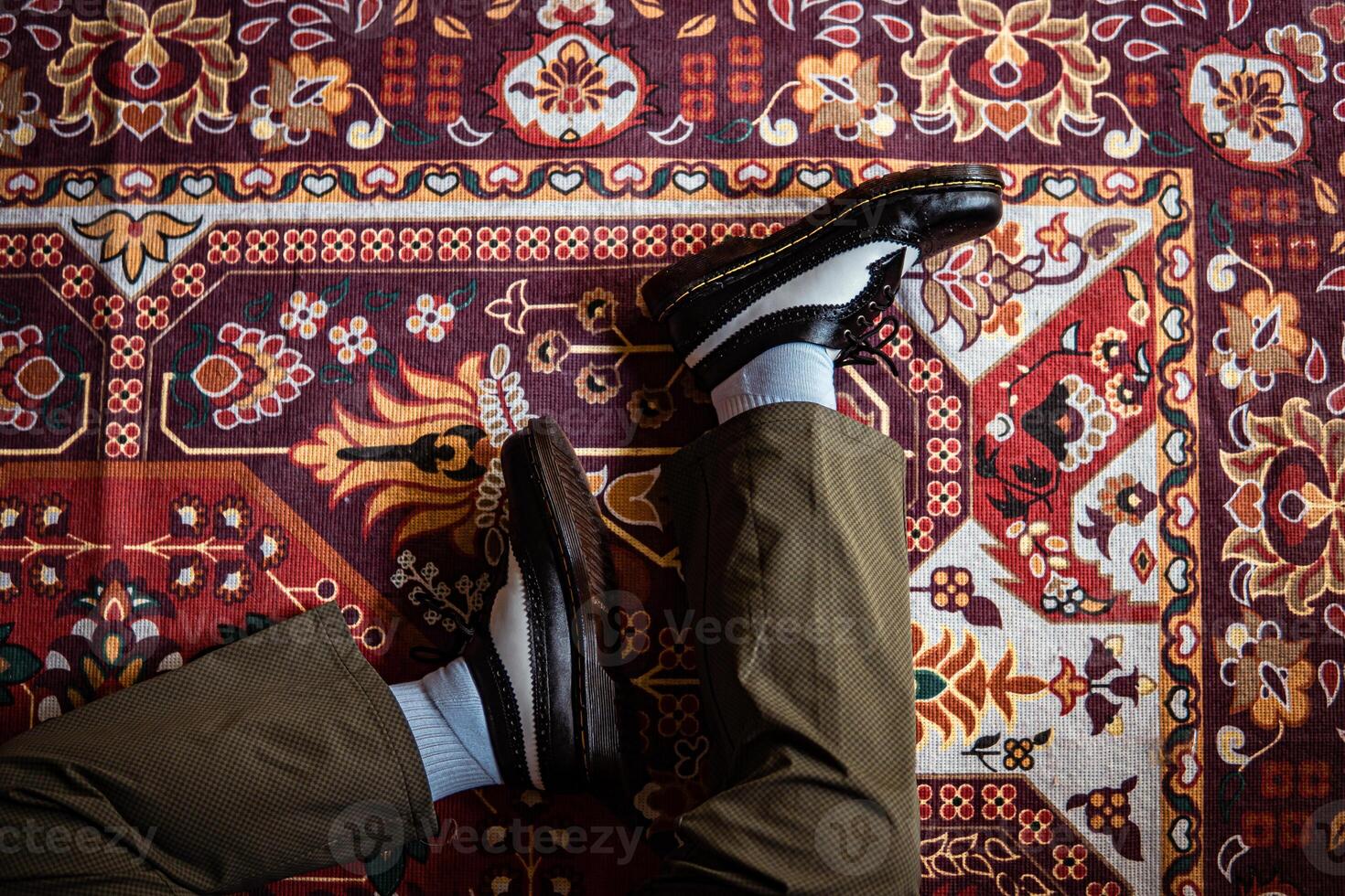Close-up view of two-tone wingtip brogue shoes made of genuine leather worn indoors on the classic red carpet. Concept photo of black and white wingtip brogue shoes with a red Turkish carpet base