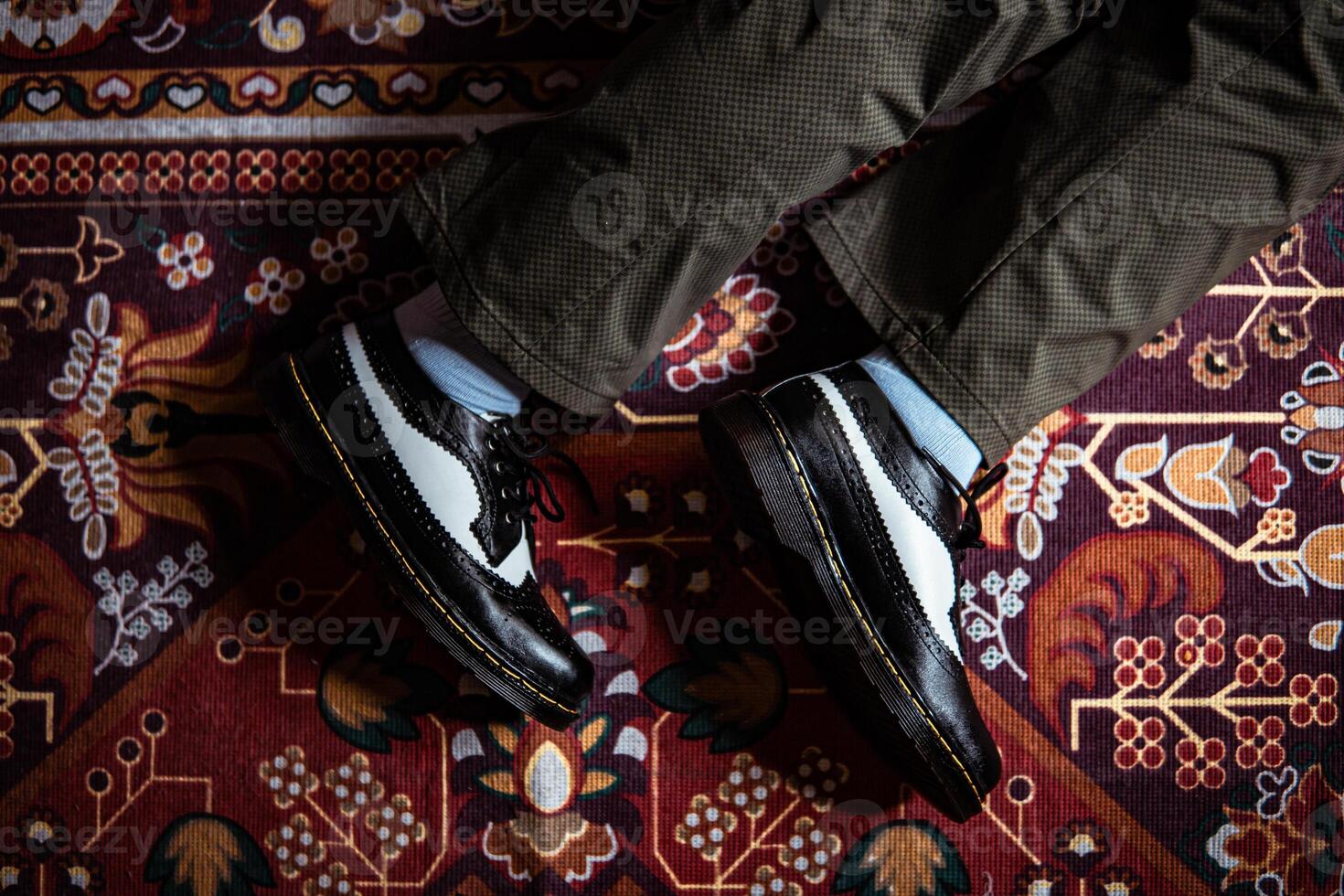 Close-up view of two-tone wingtip brogue shoes made of genuine leather worn indoors on the classic red carpet. Concept photo of black and white wingtip brogue shoes with a red Turkish carpet base