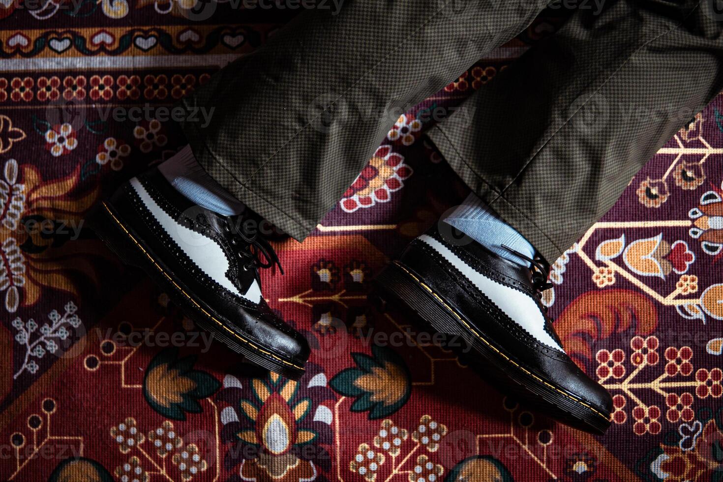 Close-up view of two-tone wingtip brogue shoes made of genuine leather worn indoors on the classic red carpet. Concept photo of black and white wingtip brogue shoes with a red Turkish carpet base