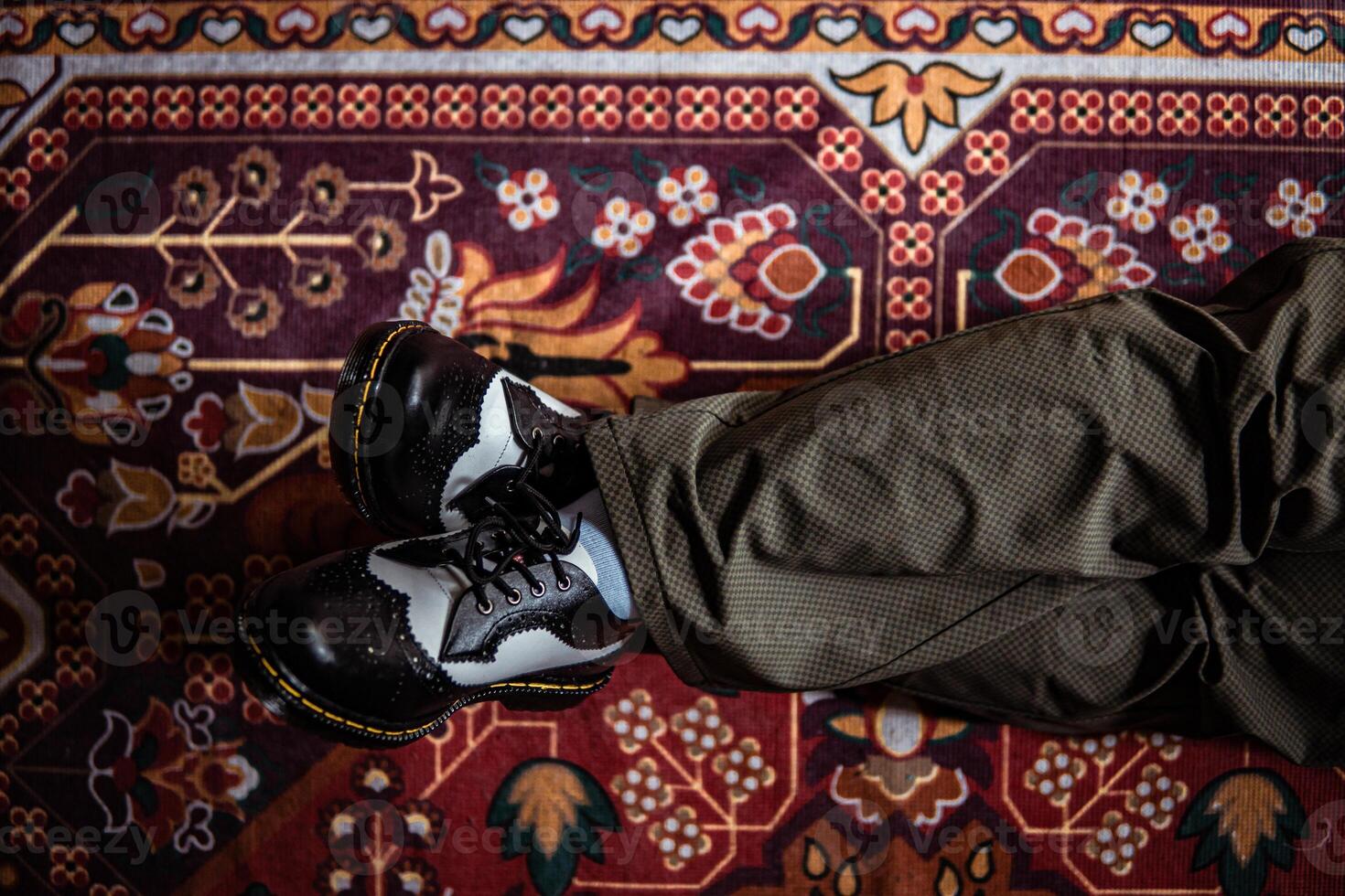 Close-up view of two-tone wingtip brogue shoes made of genuine leather worn indoors on the classic red carpet. Concept photo of black and white wingtip brogue shoes with a red Turkish carpet base