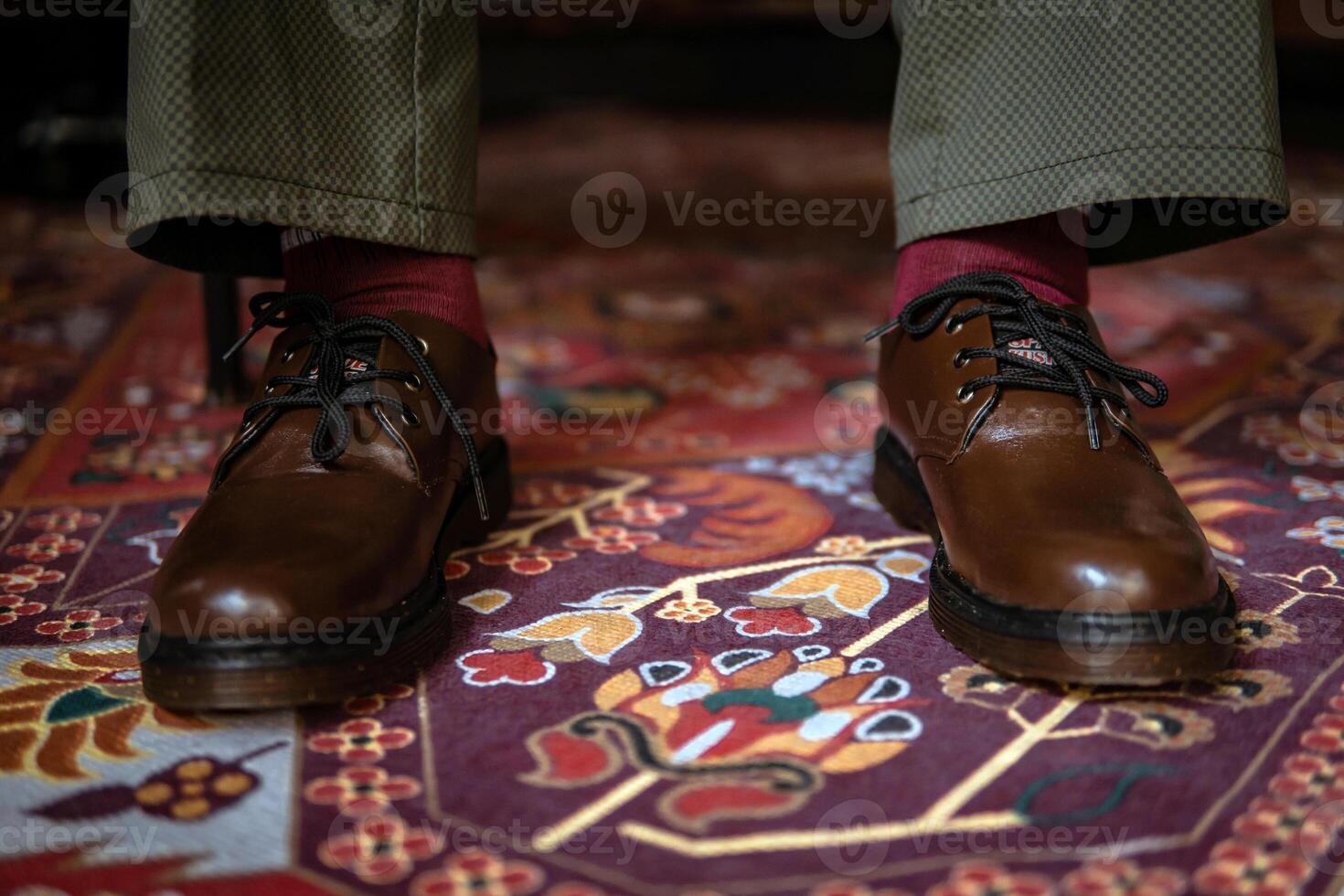 Close-up of a product concept photo of 3-hole boots made of genuine leather. Vintage shoes worn indoors on a classic red carpet. Shiny and elegant brown boots on the Turkish red carpet