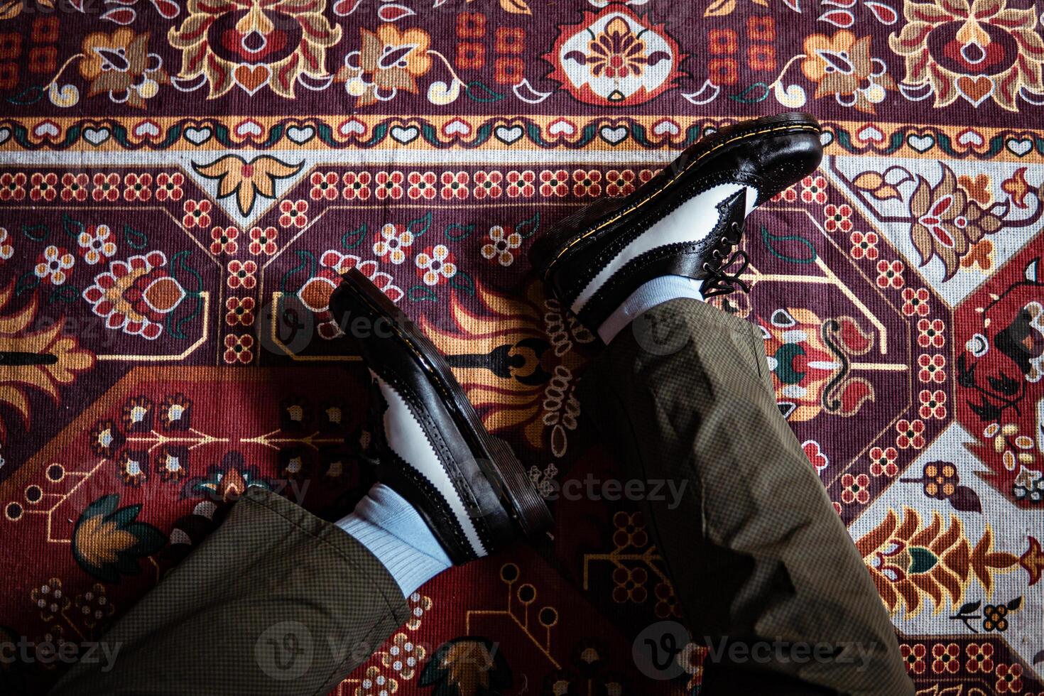 Close-up view of two-tone wingtip brogue shoes made of genuine leather worn indoors on the classic red carpet. Concept photo of black and white wingtip brogue shoes with a red Turkish carpet base
