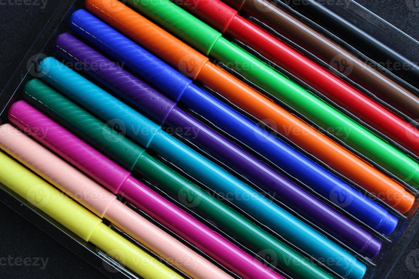 A set of twelve colored felt-tip pens in a transparent box on a black background photo