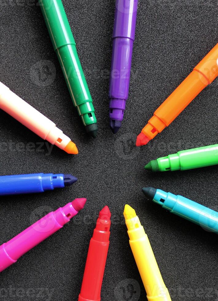 Open felt tip pens of different colors in the shape of a star lie on a black background vertical photo