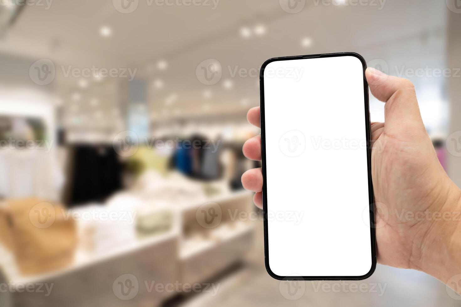 Hand holding blank screen smartphone for copy space on blurred clothing store. e-commerce app shopping mockup. social media, payment and shopping online concept. fashion and technology. photo