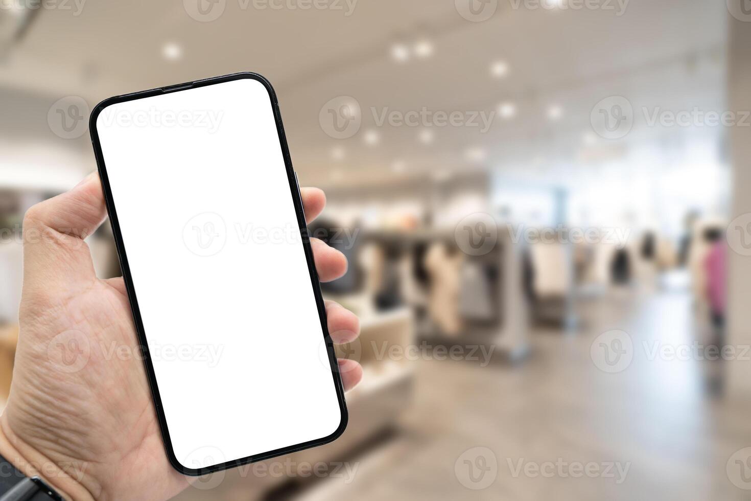 Hand holding blank screen smartphone for copy space on blurred clothing store. e-commerce app shopping mockup. social media, payment and shopping online concept. fashion and technology. photo